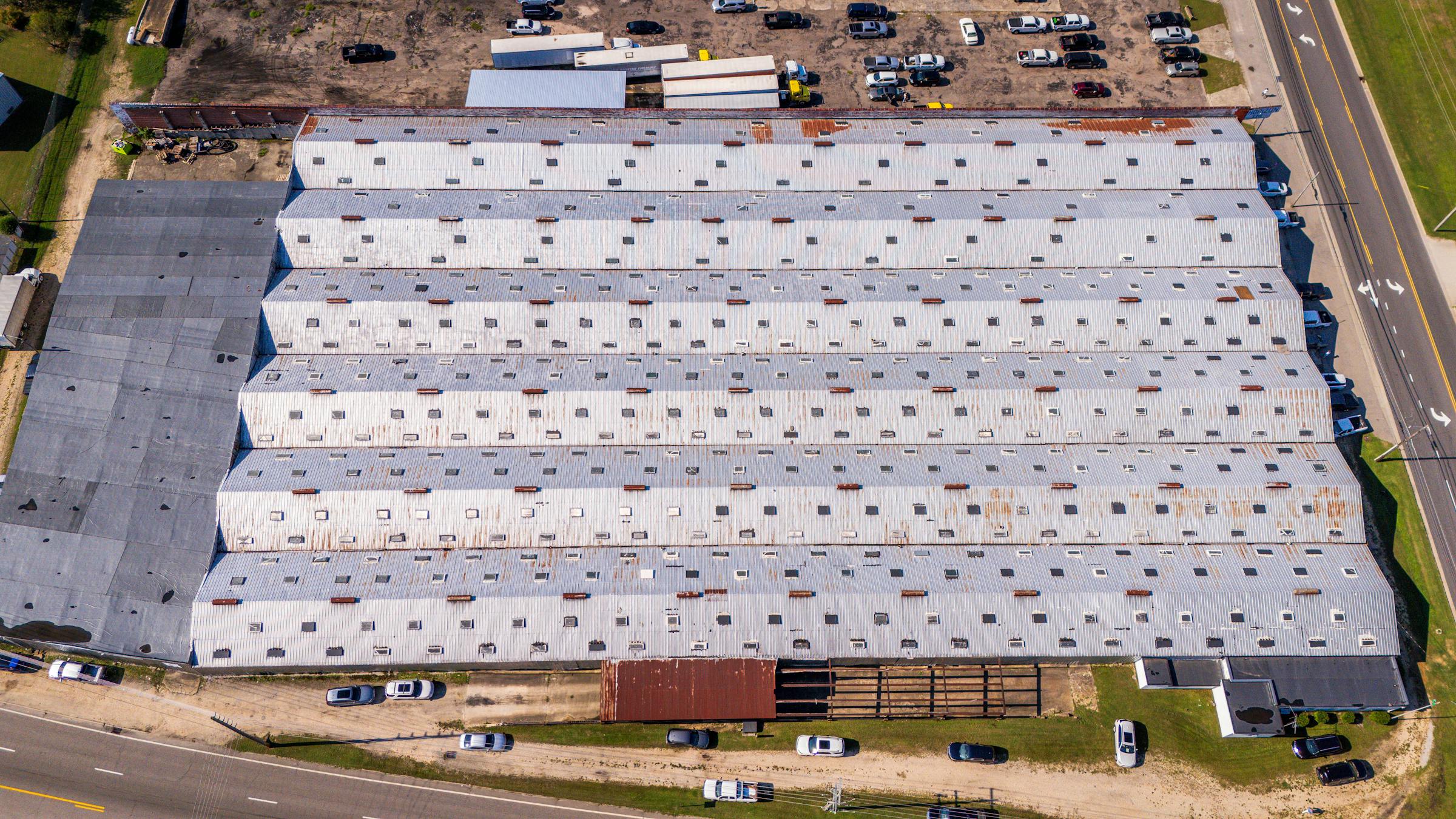 Aerial view of a large aging commercial building with a weathered low-slope roof — the kind of roof system most owners cannot identify until it starts leaking