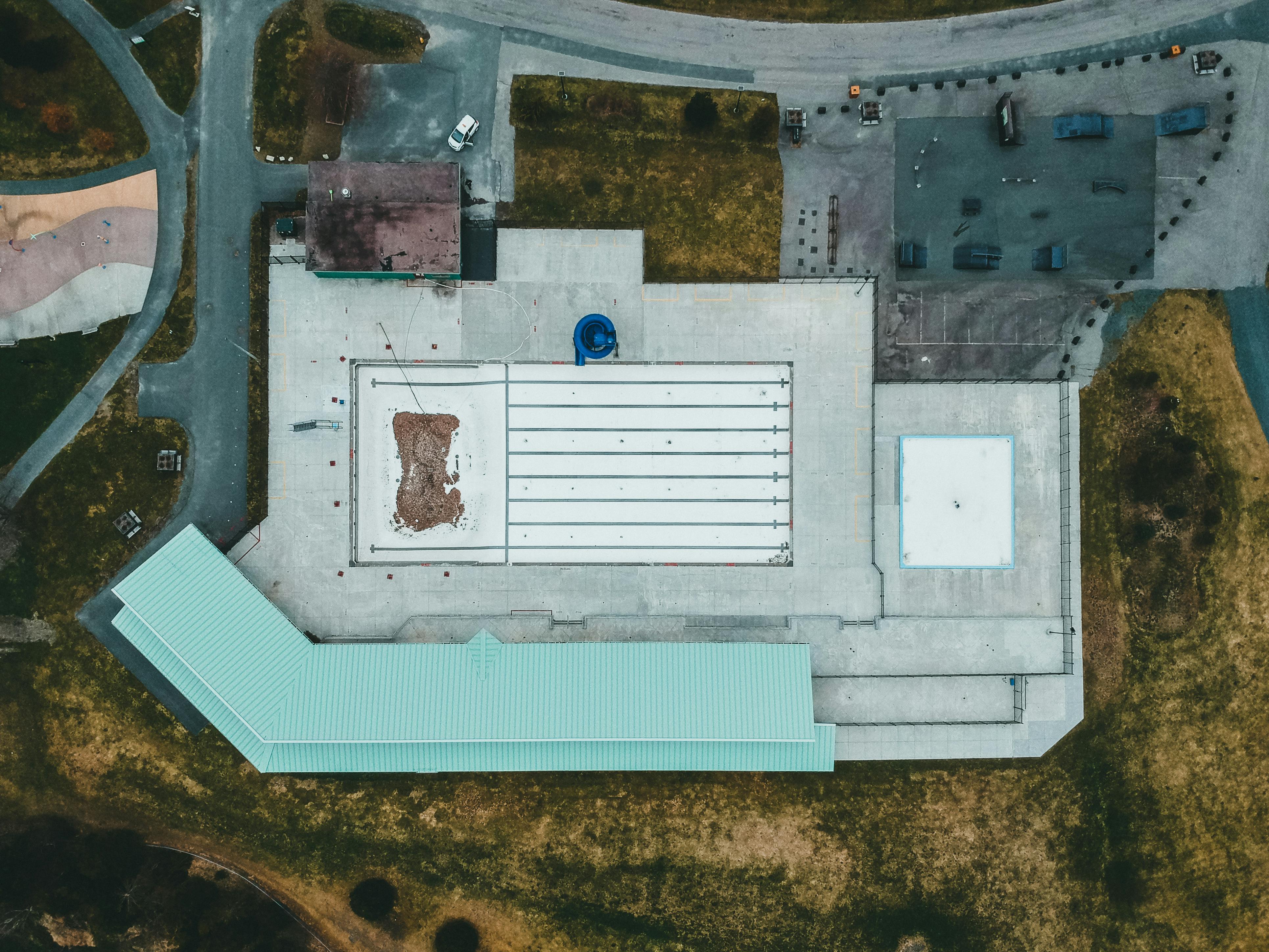 Aerial view of a large commercial flat roof with visible membrane staining and drainage lines — the kind of surface where ponding water accumulates and does long-term damage